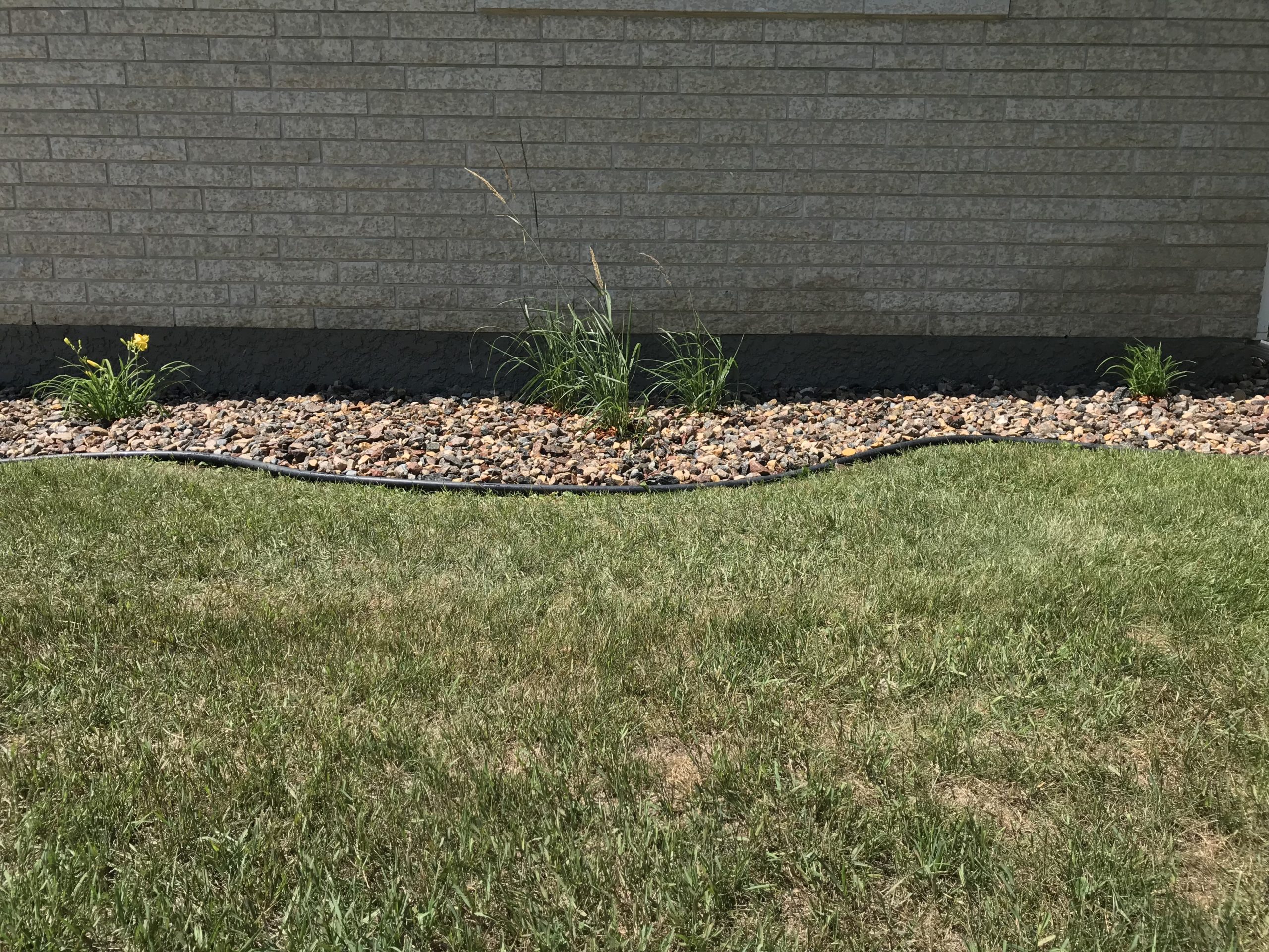 Clean river rock bed with minimal plantings and black edging installed along foundation