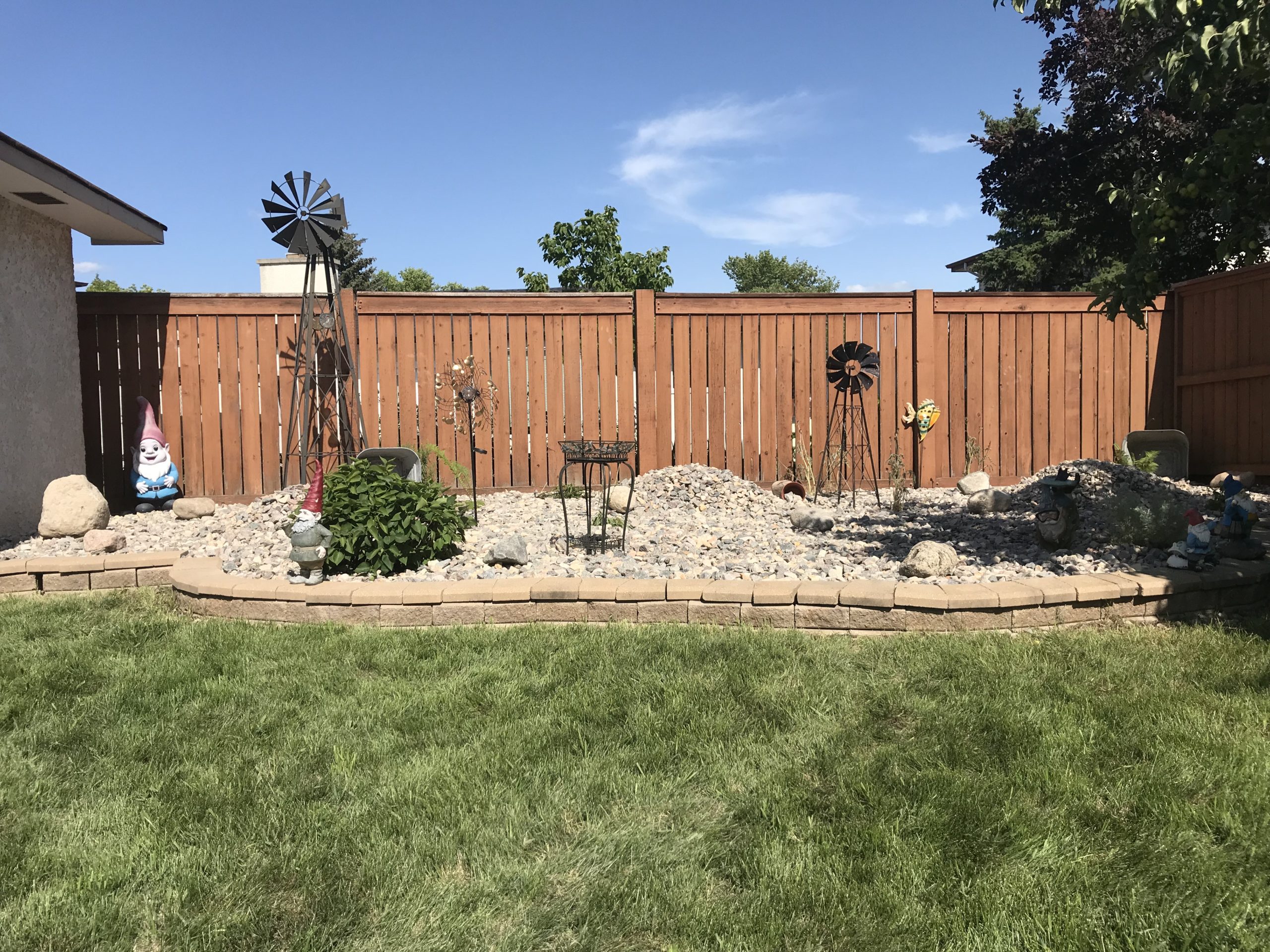 Rock-filled corner bed with decorative windmill, gnome, and low-maintenance landscaping