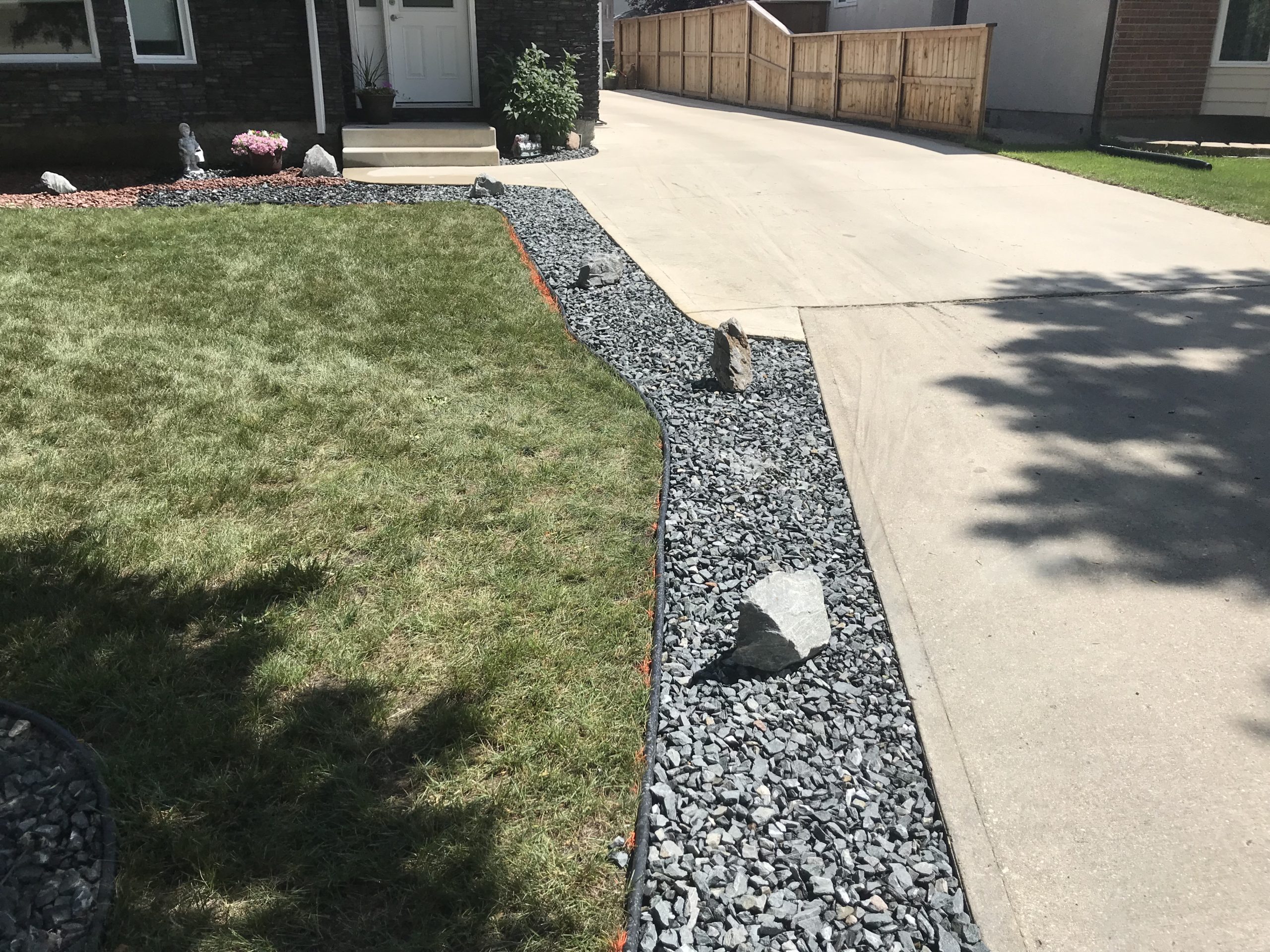 Slate rock border installed along driveway edge with boulders and edging