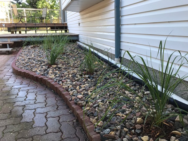 River rock bed with ornamental grasses and brick edging along foundation walkway