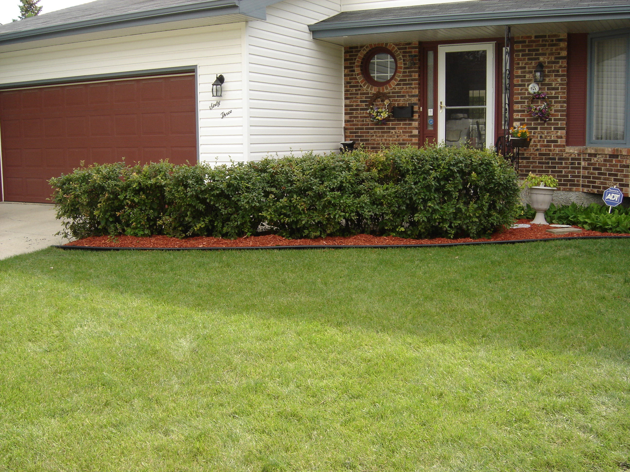 Red mulch bed with black edging installed under front hedge row