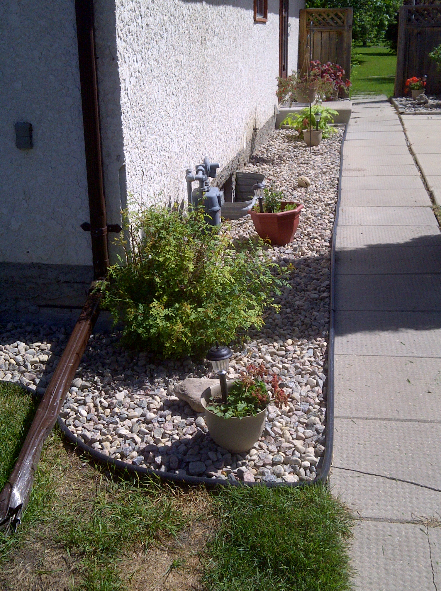 River rock pathway with plants, edging, and improved drainage along foundation