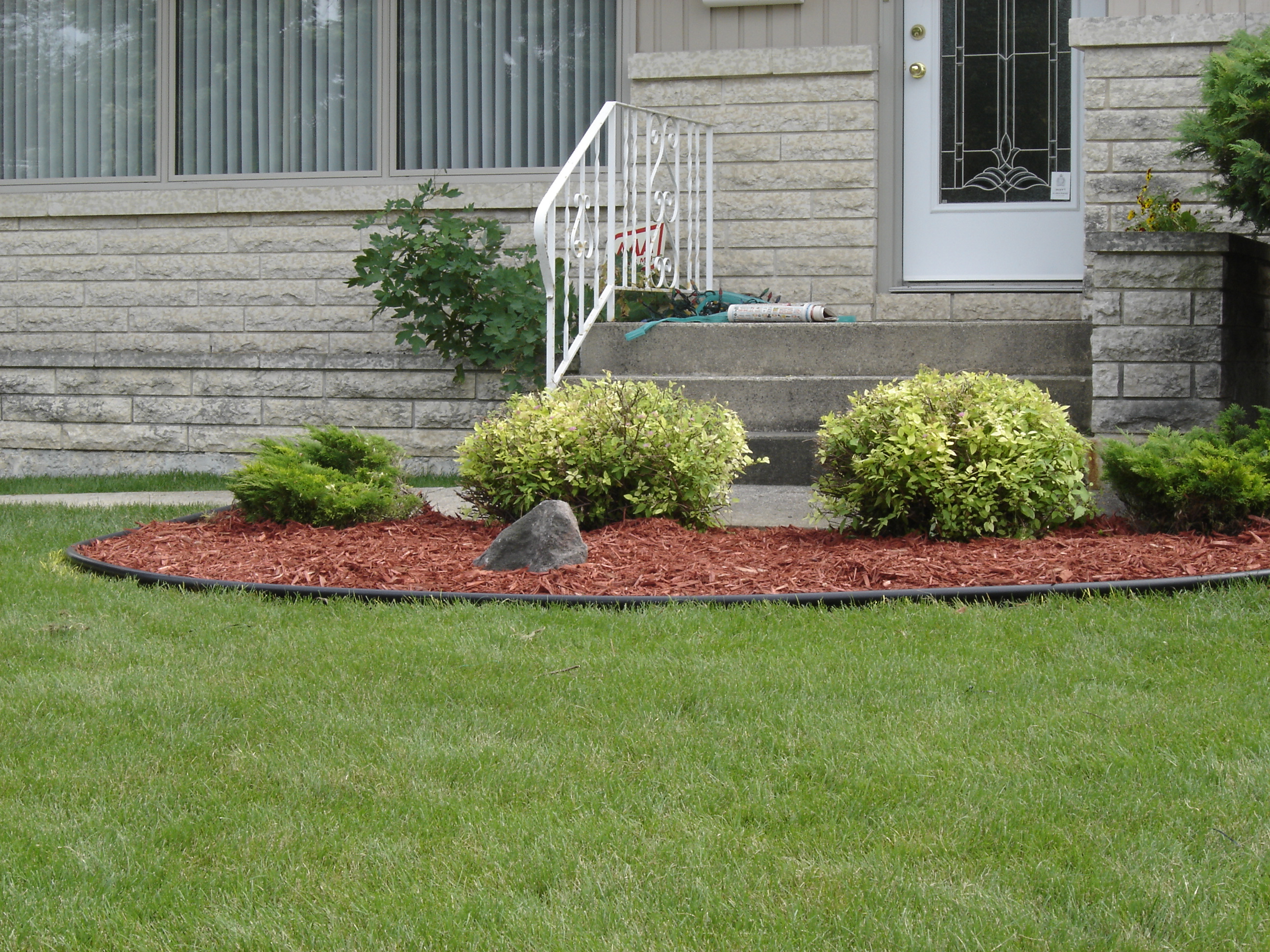 Red cedar mulch with boulder accent installed under front foundation shrubs