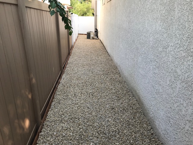 Clean gravel rock pathway installed in narrow side yard for drainage and access
